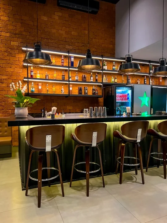 Bancada do bar com luminárias industriais e garrafas iluminadas
