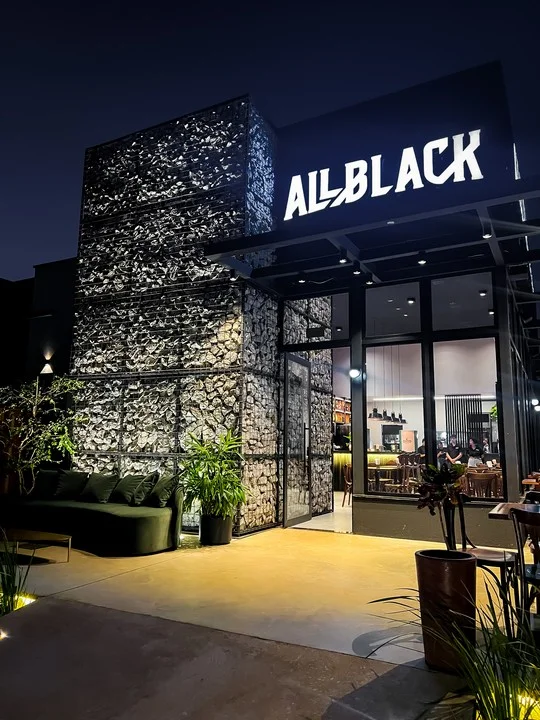 Fachada de pedra preta com o letreiro All Black aceso, à noite