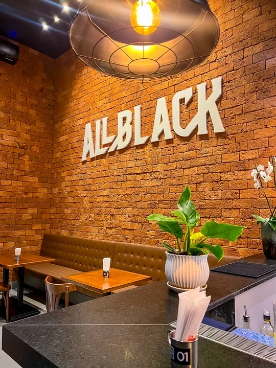 Parede de tijolo com letreiro All Black e luminária acesa